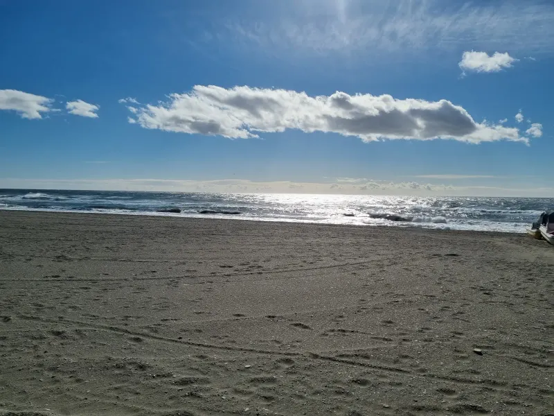 Empty sandy beach under a blue sky with a few clouds and the sea in the distance